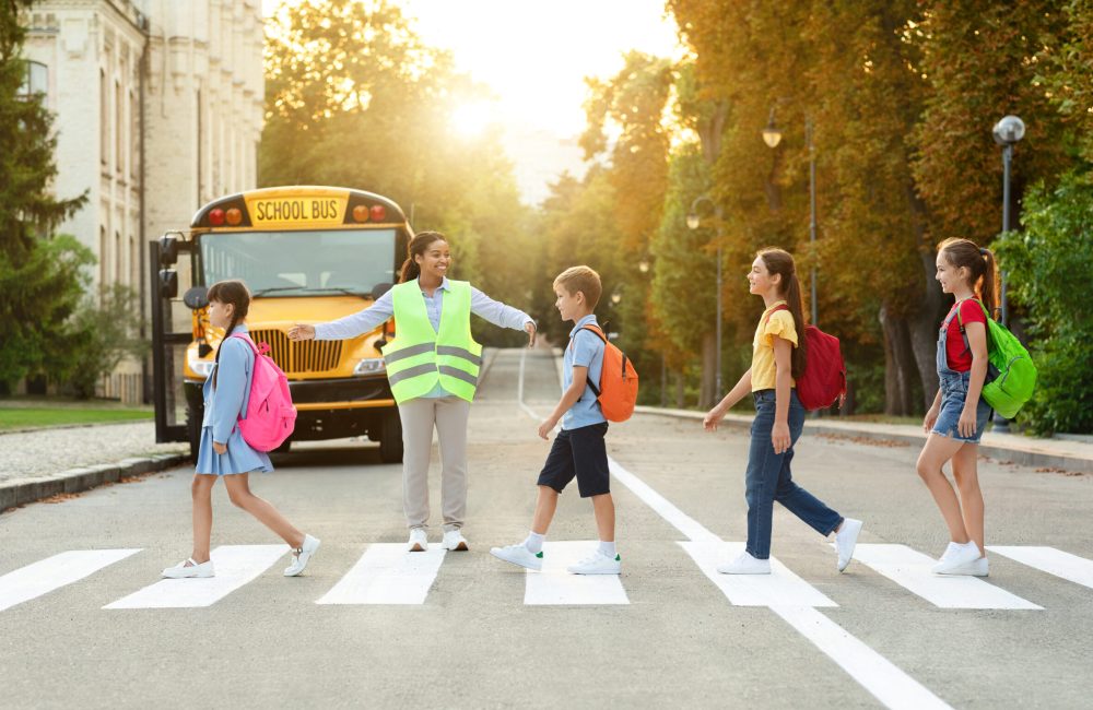 Group of children passing crosswalk on their way to school bus, diverse pupils cross the street with the crossing guard blocking traffic, boys and girls going home after classes, copy space